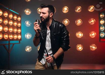 Brutal bearded singer with microphone on the stage with the decorations of lights. Brutal bearded singer with microphone on the stage