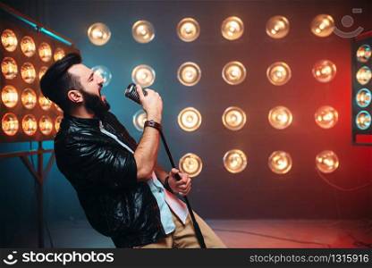 Brutal bearded singer with microphone on the stage with the decorations of lights. Brutal bearded singer with microphone on the stage