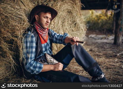 Brutal cowboy relax with cigar, haystack on background, western. Vintage male person with gun on farm, wild west culture