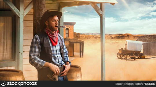 Brutal cowboy smokes a cigar at the saloon entrance, desert valley on background, western. Vintage male person with gun in country, wild west culture