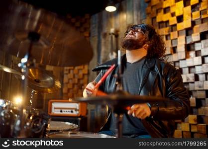 Brutal drummer behind the drum kit, music performing on stage. Rock band performance or repetition in garage, man with musical instrument, live sound performer. Brutal drummer behind the drum kit on stage