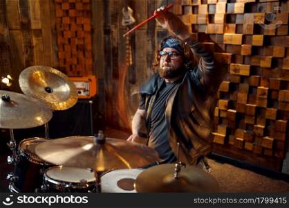 Brutal drummer behind the drum kit, music performing on stage. Rock band performance or repetition in garage, man with musical instrument, live sound performer. Brutal drummer behind the drum kit on stage