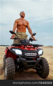Brutal man poses on atv in desert sands, quadbike racer. Male person on quad bike, sandy race on quadbike, dune safari in hot sunny day, 4x4 extreme adventure, quad-biking. Brutal man poses on atv in desert sands, quadbike