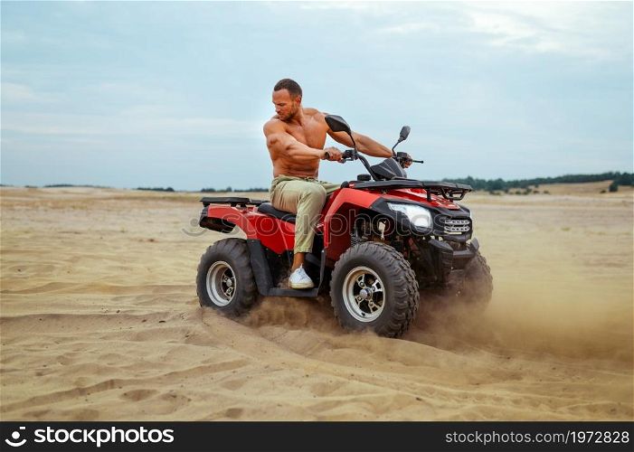 Brutal man poses on atv in desert sands, quadbike racer. Male person on quad bike, sandy race on quadbike, dune safari in hot sunny day, 4x4 extreme adventure, quad-biking. Brutal man poses on atv in desert sands, quadbike