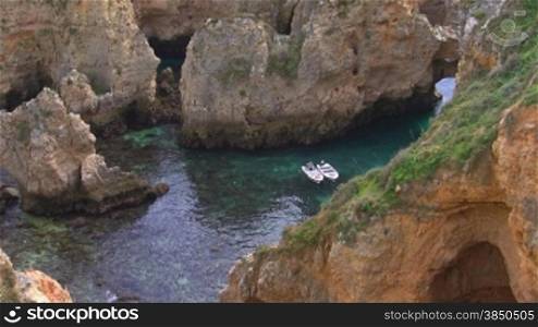 Bucht aus Steinen, flaches tnrkisblaues Meer mit Steinen / zwei Boote ankern in der kleinen Bucht; Knste der Algarve, Portugal.