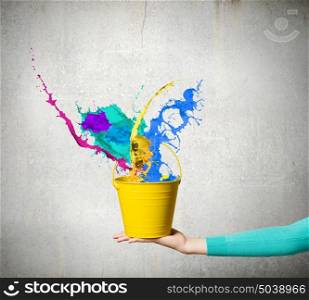 Bucket in hand. Close up of woman hand holding bucket with colorful splashes