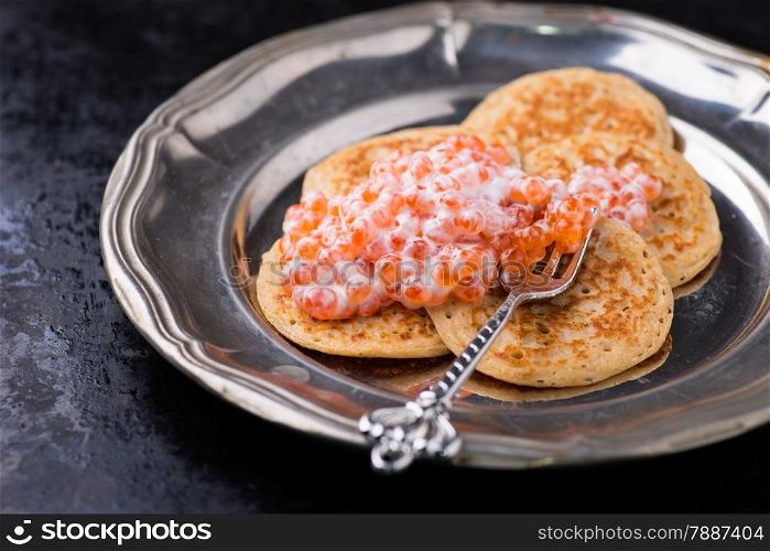 Buckwheat blini with red caviar and sour cream on metal plate, selective focus