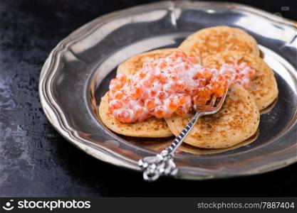 Buckwheat blini with red caviar and sour cream on metal plate, selective focus