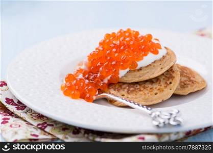 Buckwheat blini with red caviar and sour cream on white plate, selective focus