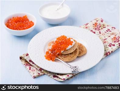 Buckwheat blini with red caviar and sour cream on white plate, selective focus