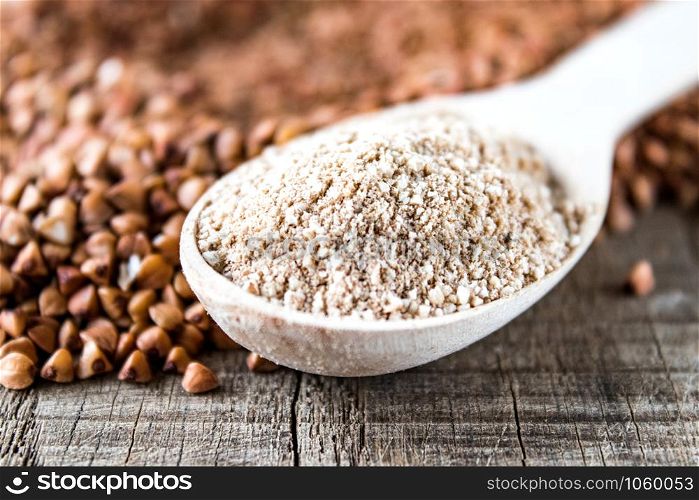 Buckwheat flour in a wooden spoon on a pile of roasted buckwheat. A pile of buckwheat flour.