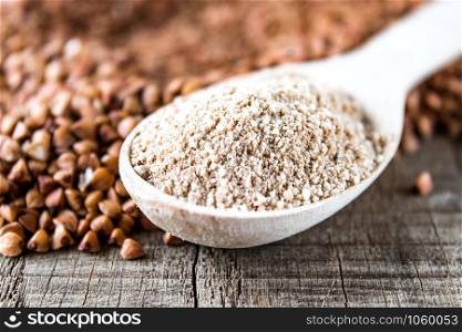 Buckwheat flour in a wooden spoon on a pile of roasted buckwheat. A pile of buckwheat flour.