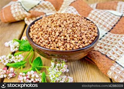 Buckwheat in a bowl with a flower buckwheat and a napkin on a wooden boards background