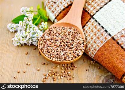 Buckwheat in a spoon with flower buckwheat, brown doily on a wooden boards background