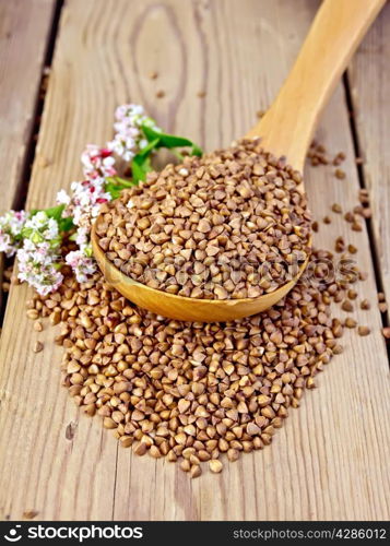 Buckwheat in a wooden spoon with flower buckwheat on a wooden boards background