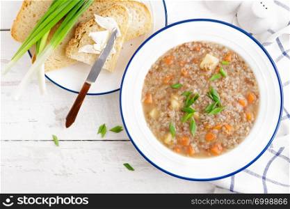 Buckwheat soup with carrot and potato on white wooden rustic table. Healthy vegetarian food, top view