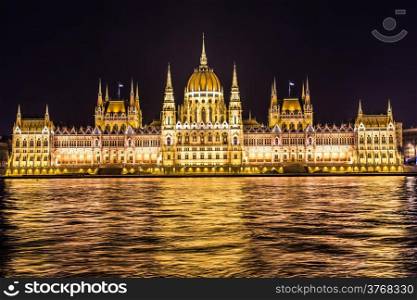 Budapest Parliament in Hungary at night, reflections on the Danube river waters.