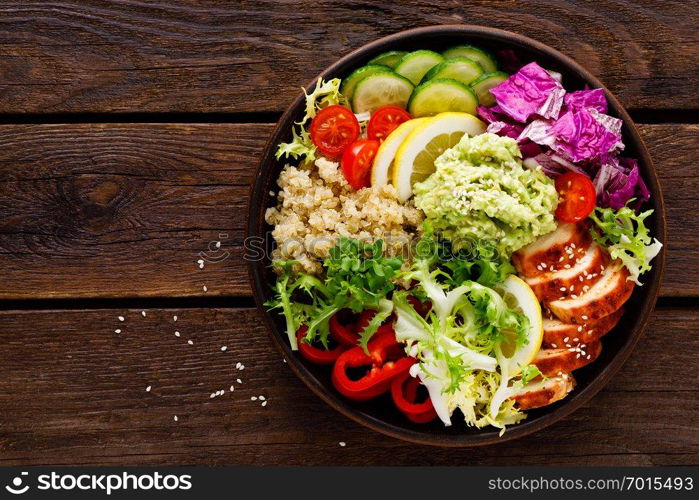 Buddha bowl dish. Healthy balanced lunch with quinoa, grilled chicken meat, lettuce salad, pepper, cucumber, tomato and avocado guacamole with lemon