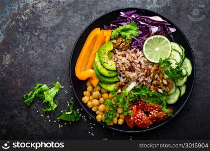 Buddha bowl dish with brown rice, avocado, pepper, tomato, cucumber, red cabbage, chickpea, fresh lettuce salad and walnuts. Healthy vegetarian eating, super food. Top view