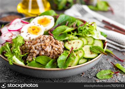 Buddha bowl dish with buckwheat porridge, boiled egg, fresh vegetable salad of radish, cucumber, lettuce and chard leaves. Healthy lunch menu