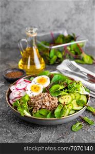Buddha bowl dish with buckwheat porridge, boiled egg, fresh vegetable salad of radish, cucumber, lettuce and chard leaves. Healthy lunch menu