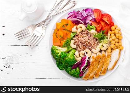 Buddha bowl dish with chicken fillet, brown rice, pepper, tomato, broccoli, onion, chickpea, fresh lettuce salad, cashew and walnuts. Healthy balanced eating. Top view. White background