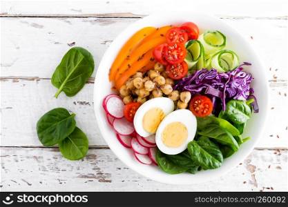 Buddha bowl salad with chickpeas, sweet pepper, tomato, cucumber, red cabbage kale, fresh radish, spinach leaves and boiled egg, healthy eating concept, top view, flat lay