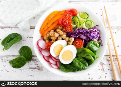 Buddha bowl salad with chickpeas, sweet pepper, tomato, cucumber, red cabbage kale, fresh radish, spinach leaves and boiled egg, healthy eating concept, top view, flat lay