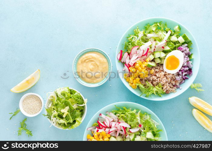 Buddha bowl with boiled egg, rice and vegetable salad of fresh lettuce, radish, cucumber, corn, onion and sesame seeds and chickpea sauce