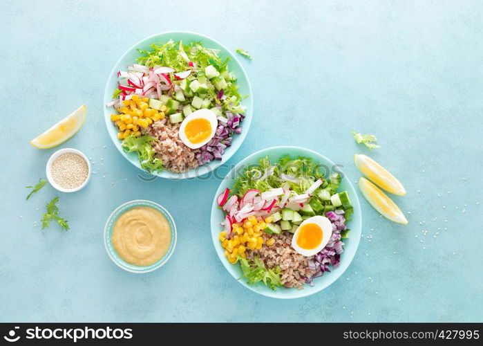 Buddha bowl with boiled egg, rice and vegetable salad of fresh lettuce, radish, cucumber, corn, onion and sesame seeds and chickpea sauce