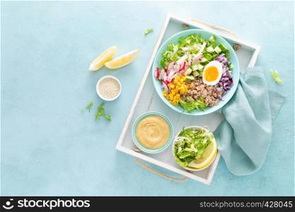 Buddha bowl with boiled egg, rice and vegetable salad of fresh lettuce, radish, cucumber, corn, onion and sesame seeds and chickpea sauce