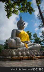 Buddha statue sitting on the rock with forest tree and blue sky background