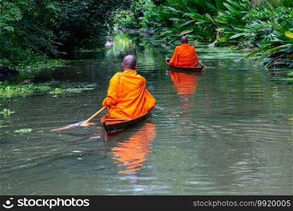 Buddhist monks paddle boat in the canal. Two monks row the small wooden boat in a canal to receive alms from Thai people in the morning.