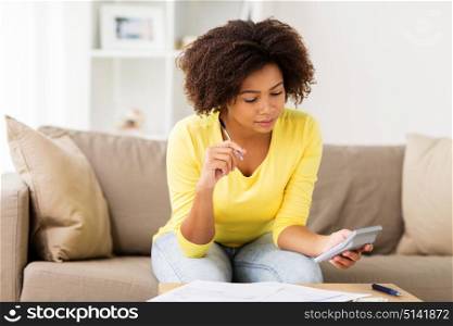 budget, finances and people concept - african american woman with papers and calculator counting money at home. african woman with papers and calculator at home