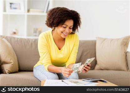 budget, finances and people concept - happy african american woman with papers and calculator counting money at home. african woman with papers and calculator at home