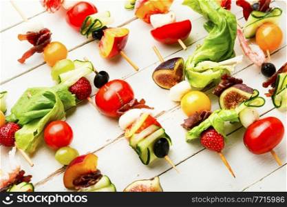 Buffet appetizer of shrimps, jamon, fruits and vegetables on wooden skewers. Easy snack from vegetables, fruits, meat and seafood