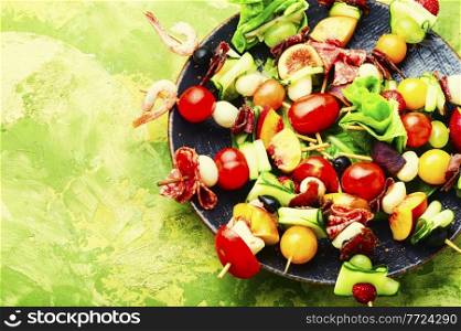 Buffet appetizer of shrimps, jamon, fruits and vegetables on wooden skewers.Copy space. Easy snack from vegetables, fruits, meat and seafood