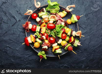 Buffet appetizer of shrimps, jamon, fruits and vegetables on wooden skewers.Flat lay. Easy snack from vegetables, fruits, meat and seafood