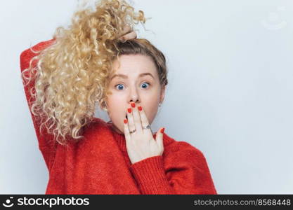 Bugged eyed emotional funny blonde female with pony tail and curly hair, covers mouth with hand, doesn t expect to hear shocking news from friend, isolated over white background. Omg concept