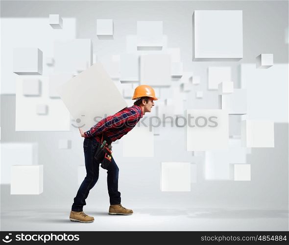 Builder among white cubes. Young builder man in hardhat carrying white blank cube on back