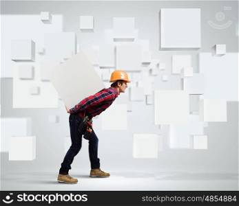 Builder among white cubes. Young builder man in hardhat carrying white blank cube on back