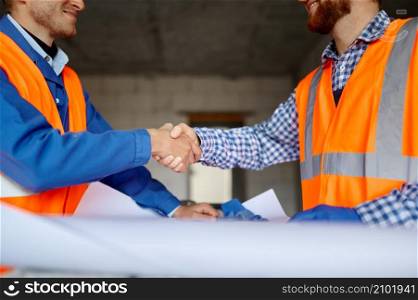 Builder and engineer handshake over paper blueprint after finish agreement. Side view closeup. Builder and engineer handshake over paper blueprint