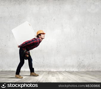 Builder carrying cube. Young builder man in hardhat carrying white blank cube on back