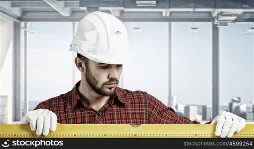 Builder checking spirit level. Engineer man in helmet indoor using level. Mixed media