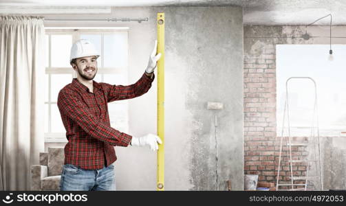 Builder checking spirit level. Engineer man in helmet indoor using level. Mixed media