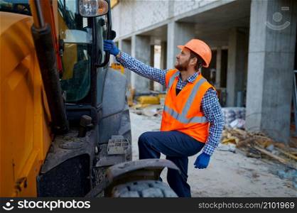 Builder contractor in helmet, uniform gets into heavy machinery cab. Construction site and industry. Builder contractor gets into heavy machinery cab