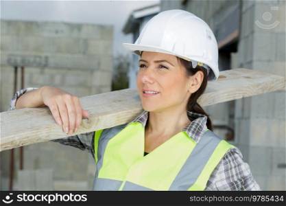 builder female apprentice carrying wood on site