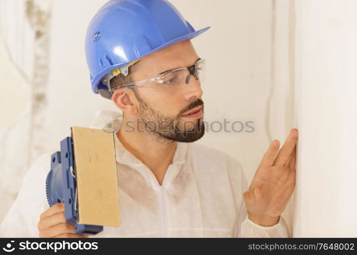 builder in hardhat sanding wall indoors