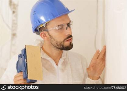 builder in hardhat sanding wall indoors