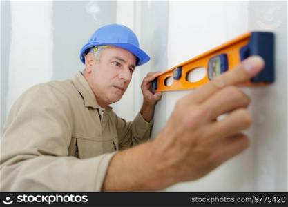 builder in uniform holding a level against the wall indoors